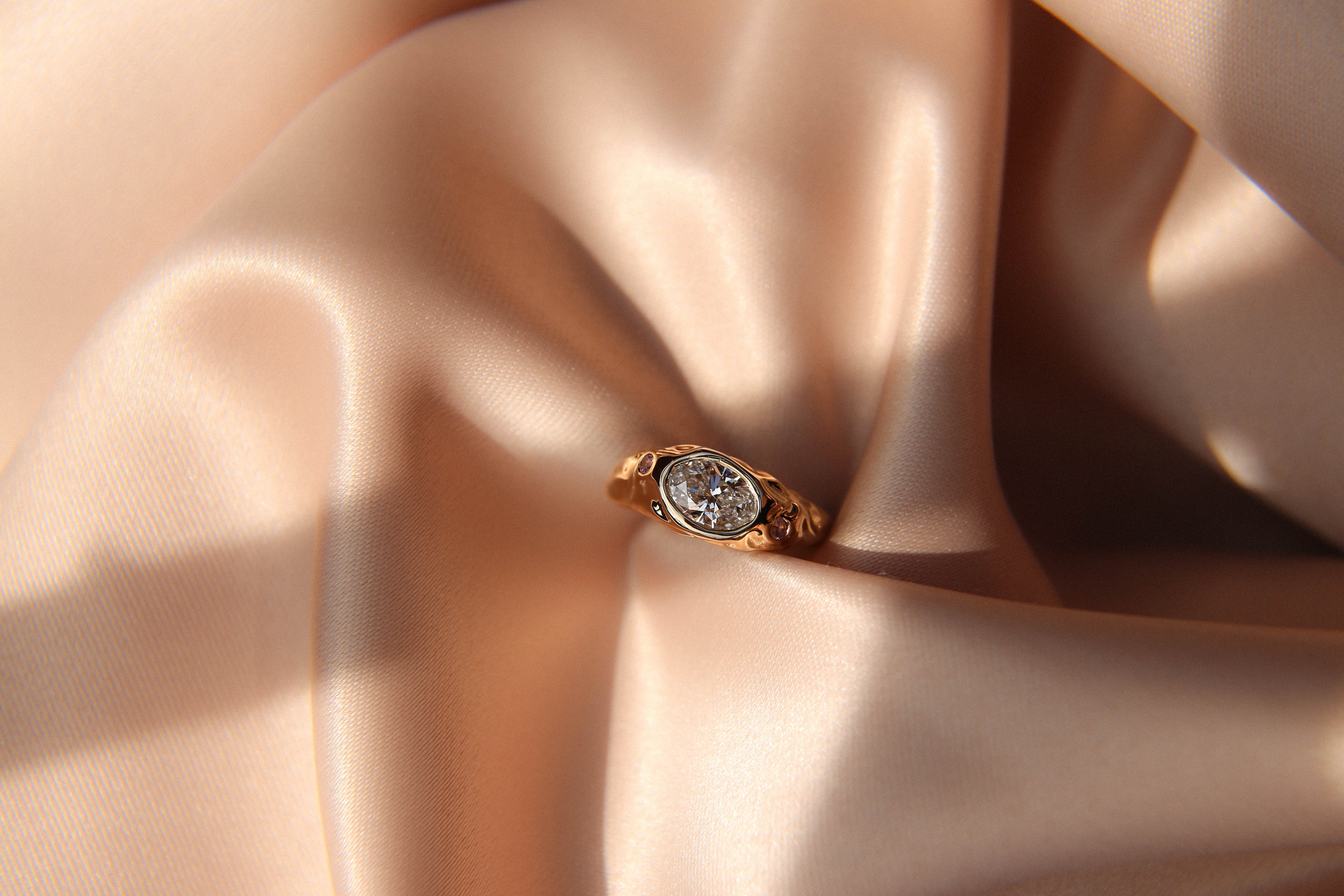 Gold ring with a diamond on a soft pink fabric background