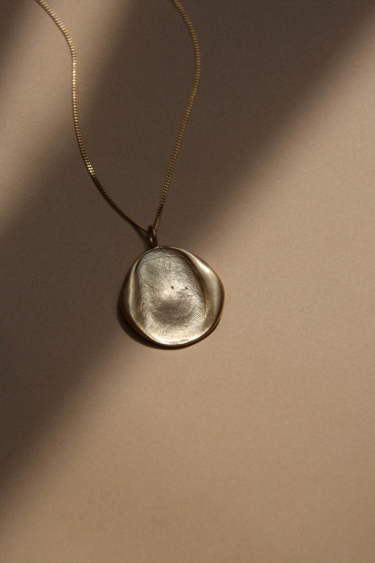 Close-up of a gold fingerprint pendant in sunlight