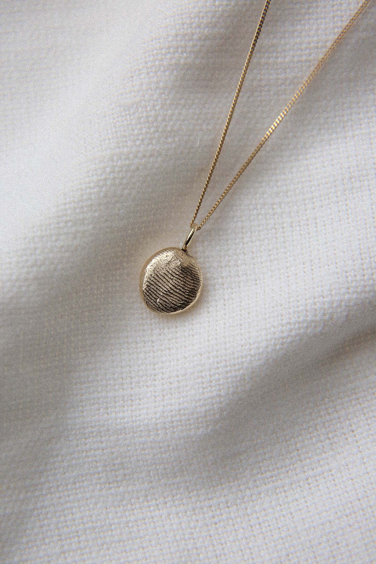 Gold fingerprint pendant on a fine chain, resting on white linen